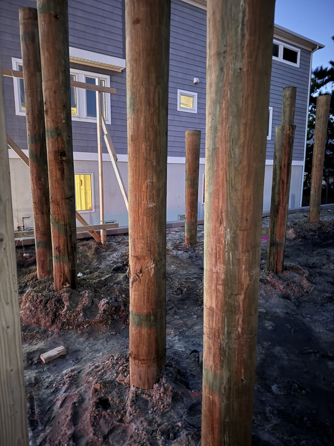 Driven timber pilings on the lot, with the neighboring homes behind