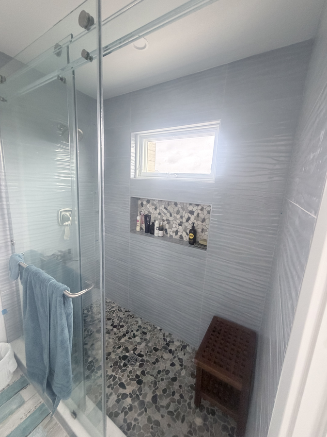 Tiled glass-enclosed shower with a pebble floor